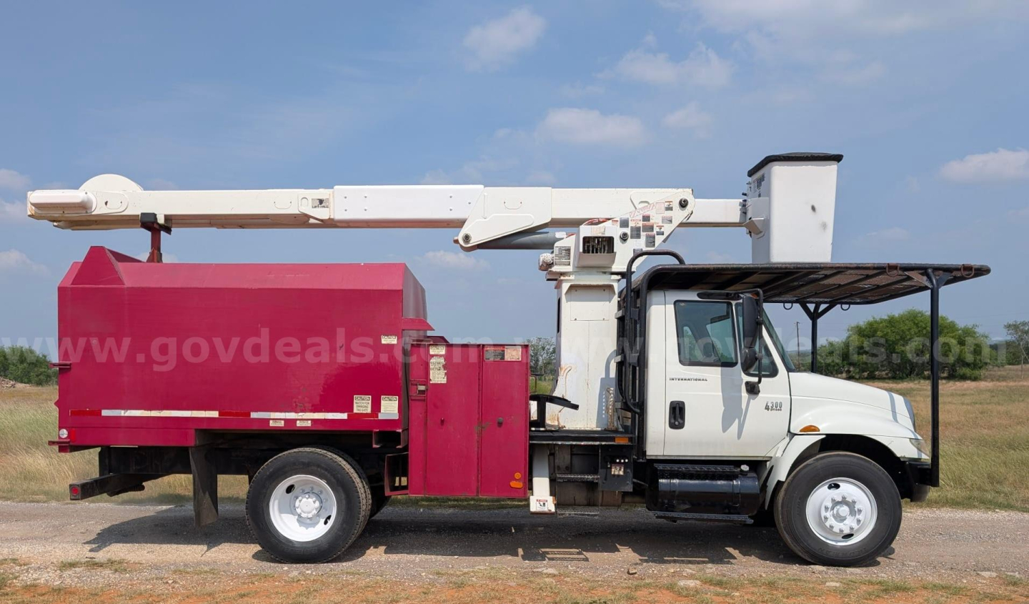 Truck with a bucket crane mounted on the chassis, white cab, red boom bucket, no visible branding readable. Side shows a label area and controls near mid-body.