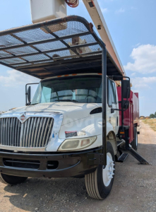 Truck front view with bucket lift elevated; International DT466 diesel engine badge visible; white cab, black bumper, side mirrors, and extended boom over cab.