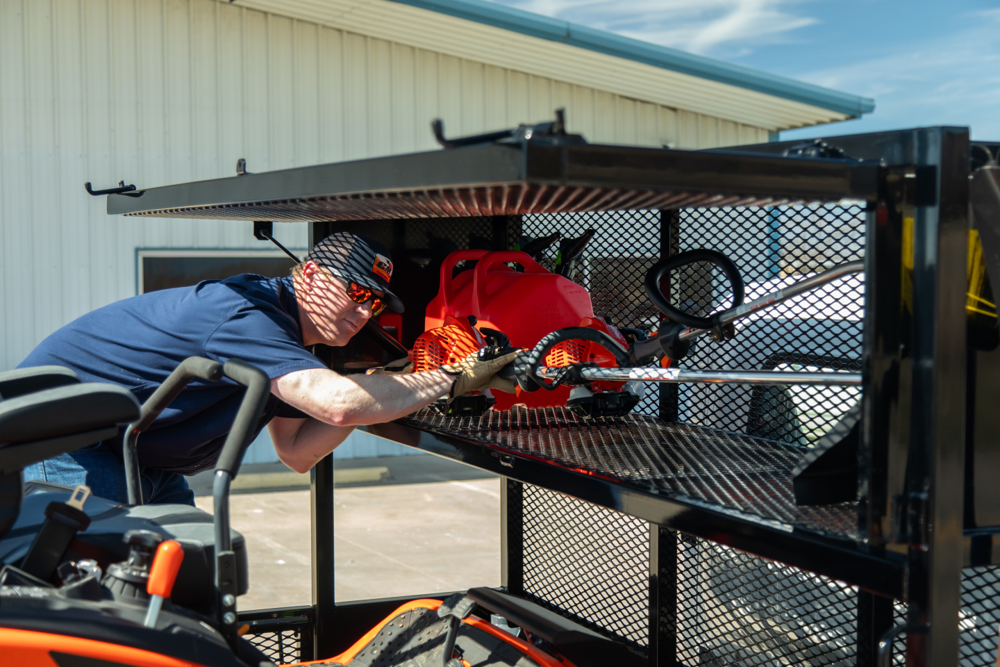 Isuzu NQR flatbed truck bay showing technician inspecting a metal tool rack with hydraulic canister and mesh guard; engine area not visible.