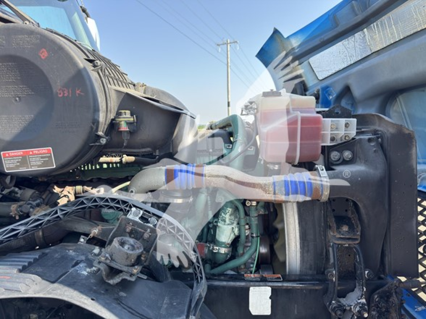 Volvo VNL interior engine bay showing coolant reservoir, hoses, and engine components with wrapped wiring and metal frame.