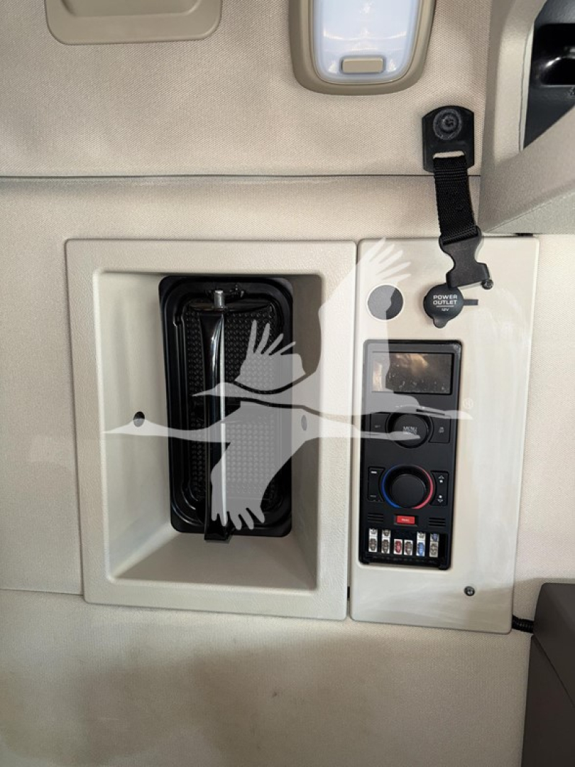 Vehicle interior showing control panel with switches, climate control, and a vent alongside a mounted lanyard and power cup holder area.