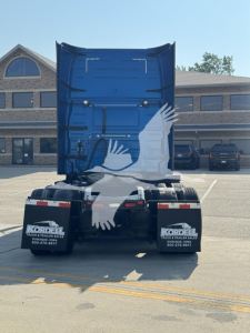 Rear view of a blue Volvo VNL truck tractor with fifth wheel, dual rear axles, mudflaps reading 'Kordell Truck & Trailer Sales' in a dealership lot.