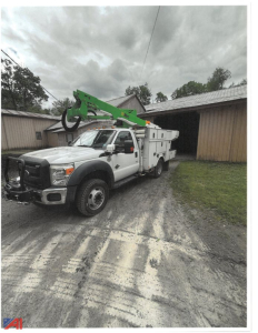 Ford F-550 bucket truck with green hydraulic boom in field, utility chassis, white service body, front bumper with grille guard.