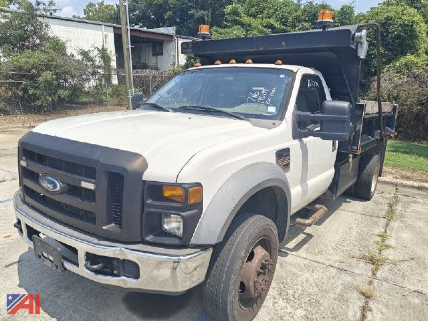 Ford F-550 Super Duty dump truck in service with dump bed raised, front grille, headlights, and orange beacon lights on cab roof.