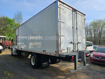 Freightliner M2 106 box truck rear view showing enclosed cargo area and dual rear doors with latches; tires and a towing hitch visible.