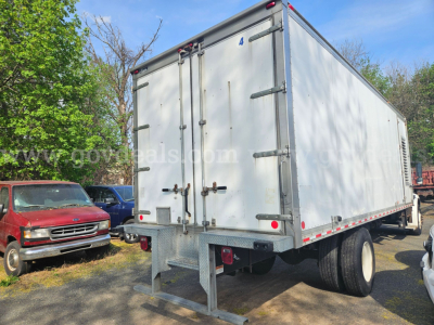 Freightliner M2 106 utility box truck rear view showing cargo box and dual rear wheels. Visible text on door corner and reflective tape along edges.