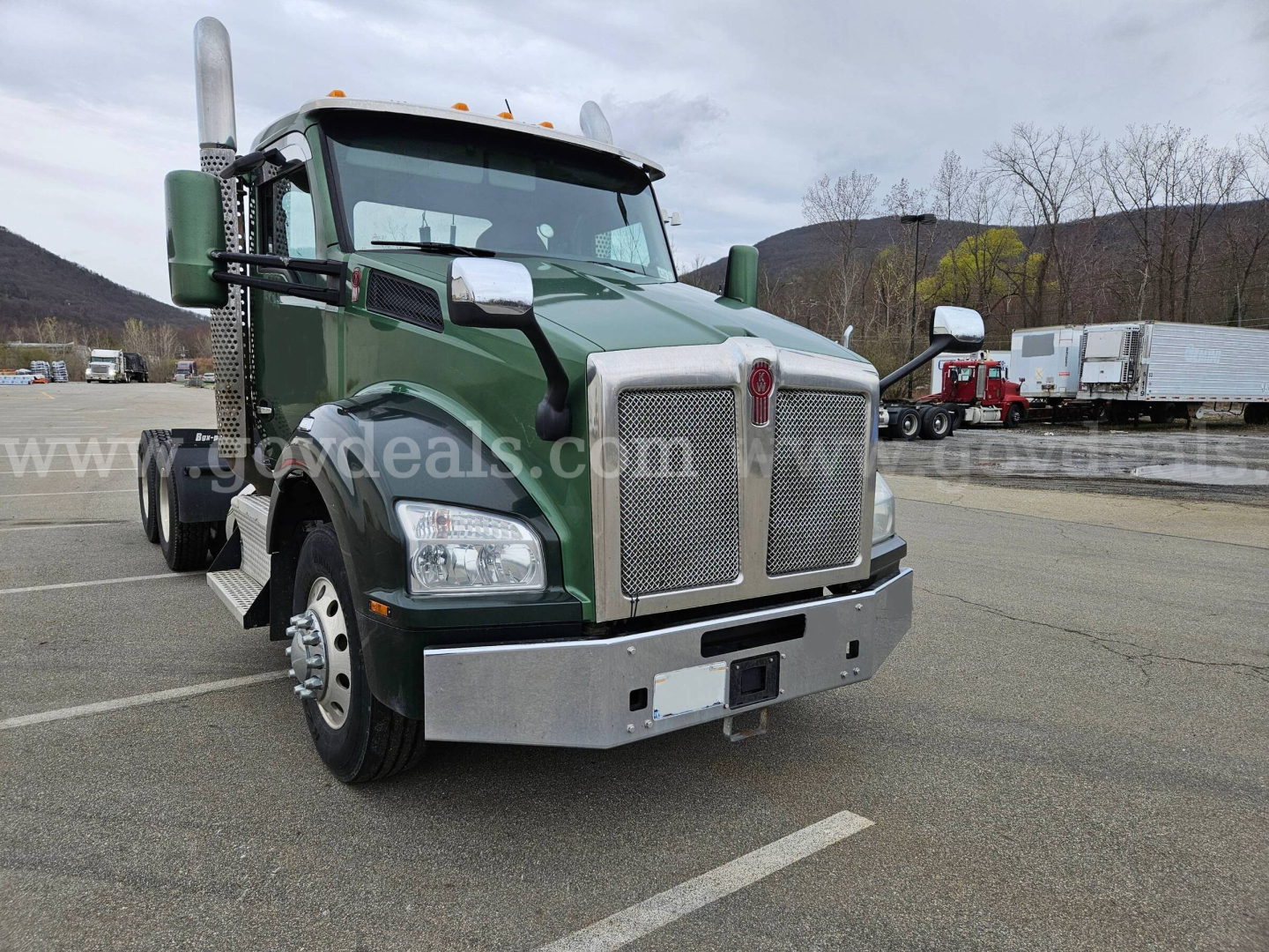 Kenworth T880 heavy-duty truck front view showing green cab and chrome grille, dual exhaust stacks, and chrome bumper.