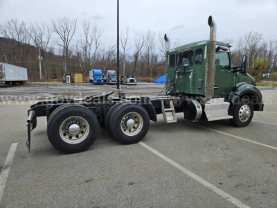 Kenworth T880 chassis and cab in a parking lot, green cab with dual rear axles and exposed exhaust stacks.