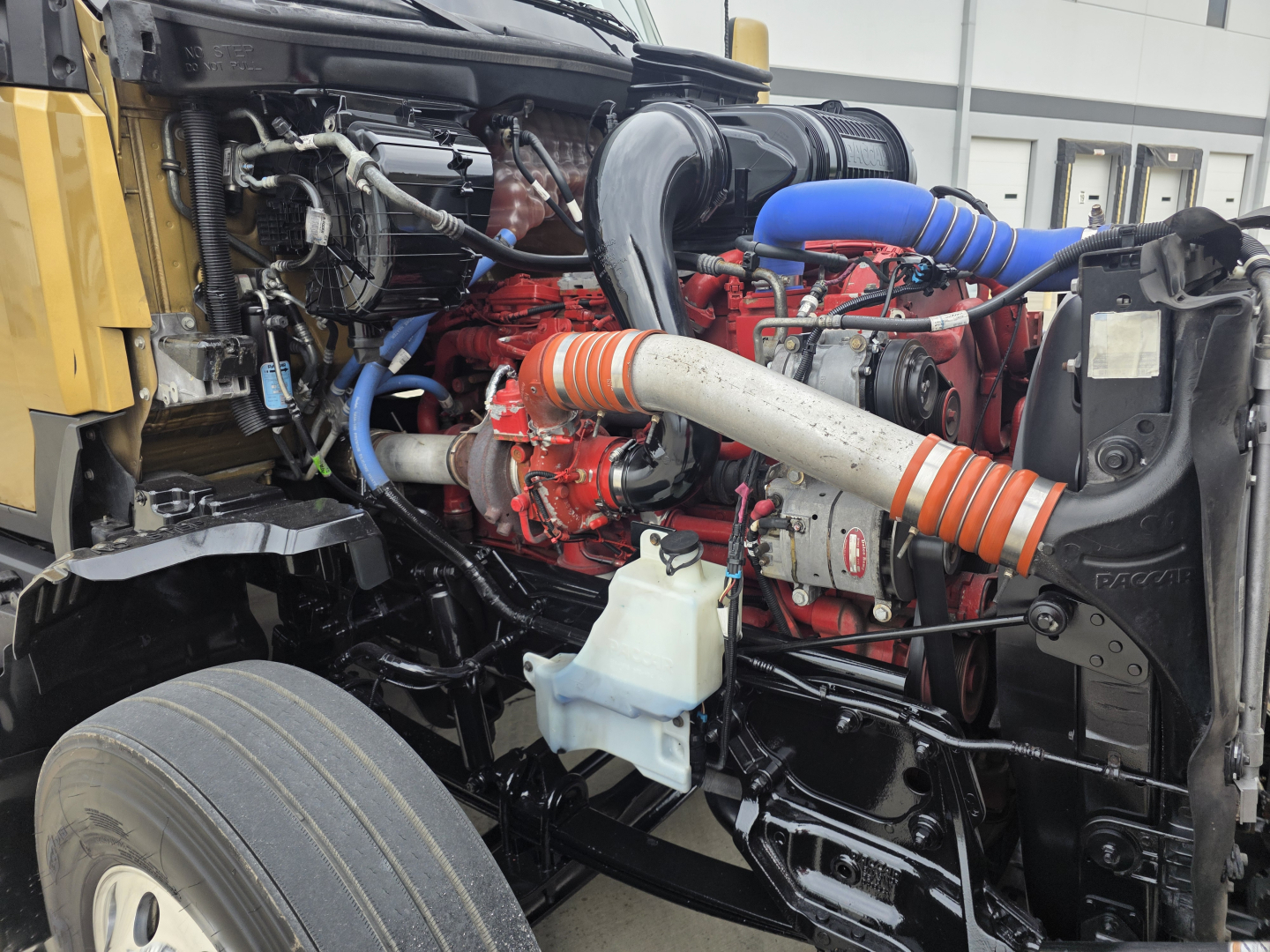 Kenworth T680 engine bay showing red engine, blue silicone hoses, white coolant reservoir, and orange-striped intake hose.