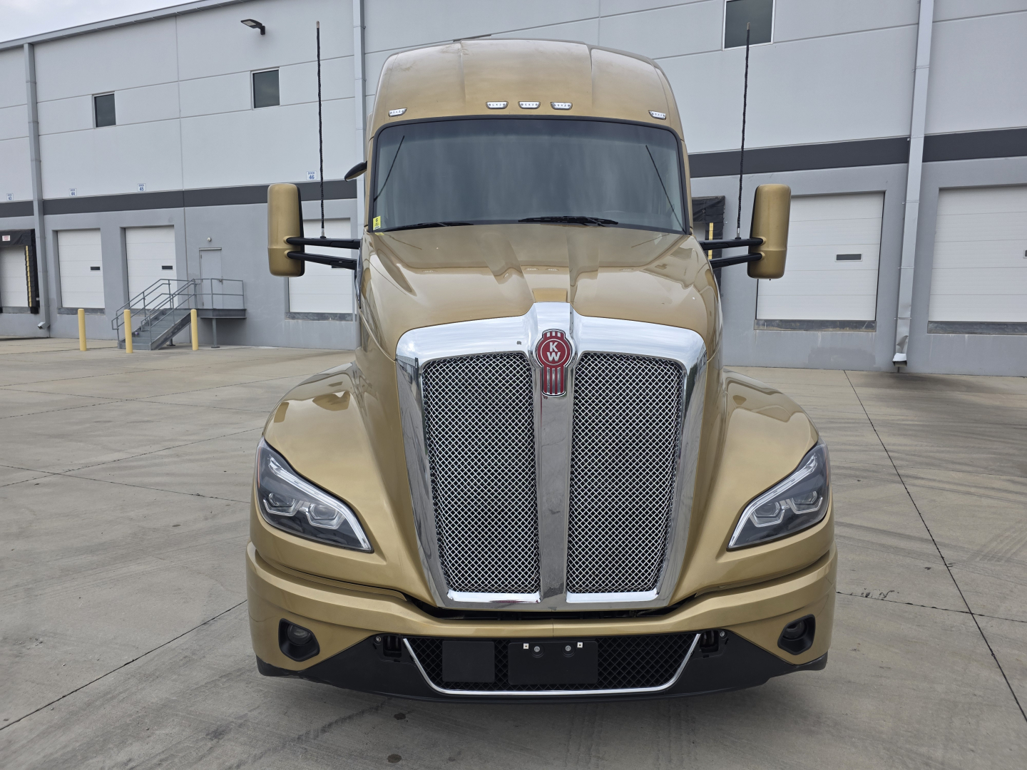 Kenworth T680 front view showing large chrome grille, dual side mirrors, tan gold paint, and factory headlights.