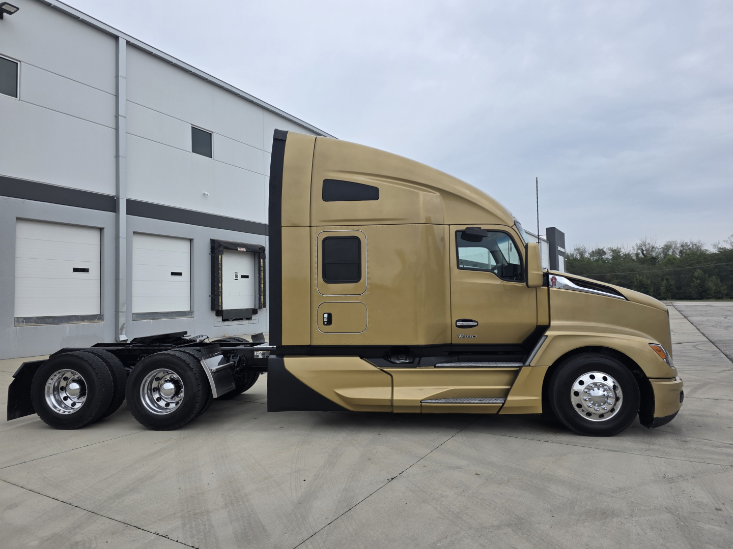Kenworth T680 2023 grayish-gold conventional sleeper tractor side view with attached trailer chassis and wheels.