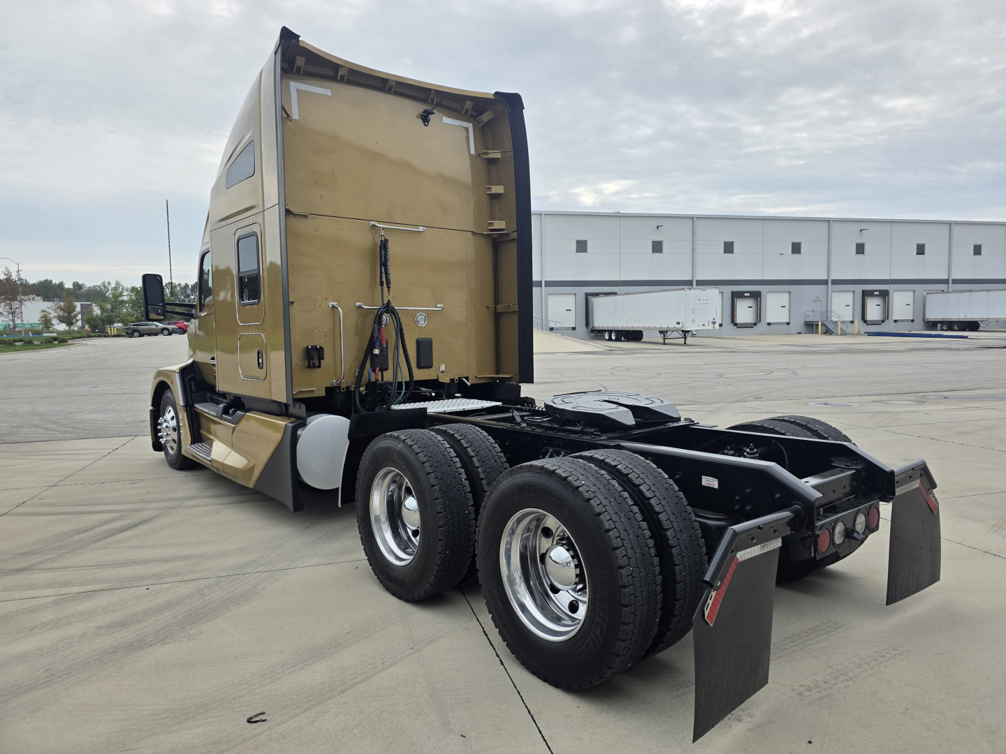 Kenworth T680 sleeper cab tractor rear view showing dual rear axles, fifth wheel, and mudflaps with beige paint.