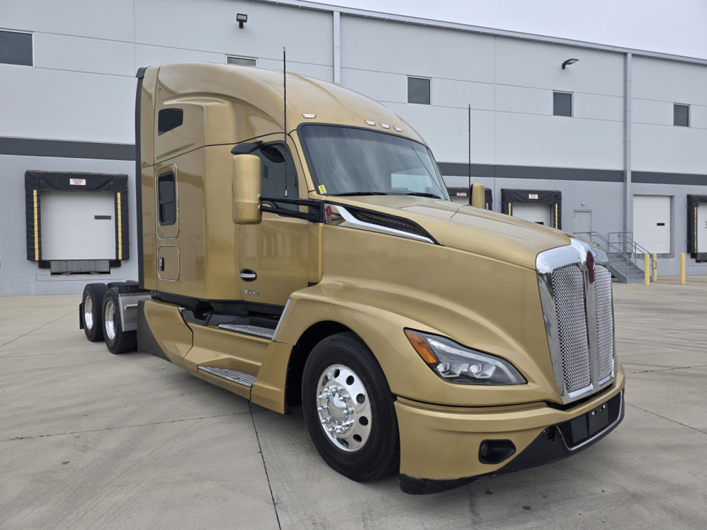 Kenworth T680 tractor cab in beige color showing front and side view with grille, headlights, and chrome wheels.