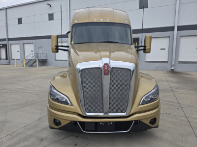 Kenworth T680 front view showing large chrome grille, dual side mirrors, tan gold paint, and factory headlights.