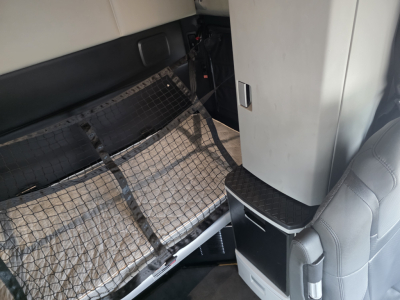 Kenworth T680 sleeper cab interior showing cargo net, storage cabinet, and seating area.