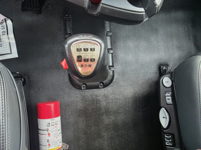 Kenworth T680 interior image showing gear shift panel and controls; visible red fire extinguisher cap and various dashboard buttons.