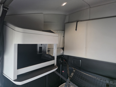 Kenworth T680 sleeper cab interior showing a side storage cabinet with white finish and a bunk area. Visible seat belt and plastic panels.