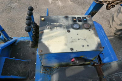 Control console with gauges and joystick levers mounted on blue truck lift equipment, shows wear and several switches and meters.