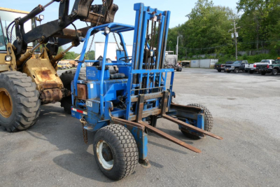 Teledyne D5000 forklift attachment in blue, compact wheeled unit with forks extended, parked in a lot near a larger machine.