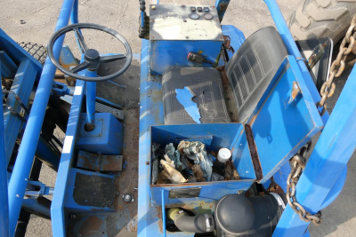 Teledyne D5000 truck lifting equipment cockpit with steering wheel, exposed wiring, worn seat cushions, open tool box containing small items, blue metal frame, and chain near controls.