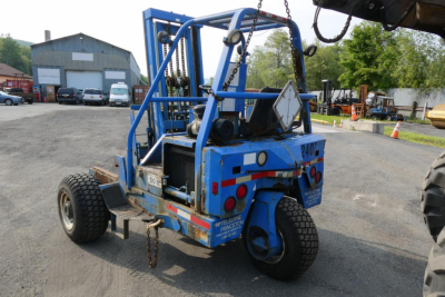 Teledyne D5000 truck-mounted lift showing blue frame and rear hitch, with tires, safety chains, and control console visible.