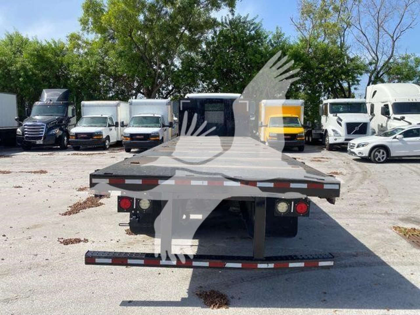Flatbed truck rear view of a 2018 Freightliner M2 106 in a used truck lot showing a flatbed, tail lights, and bumper.