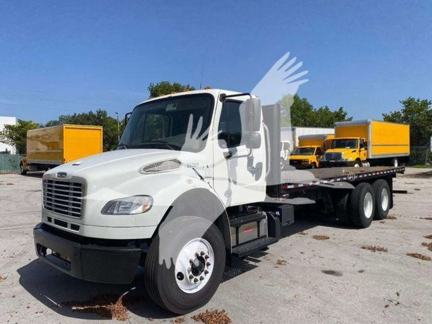 Freightliner M2 106 flatbed truck in white, front-left view, with yellow boxes in background.