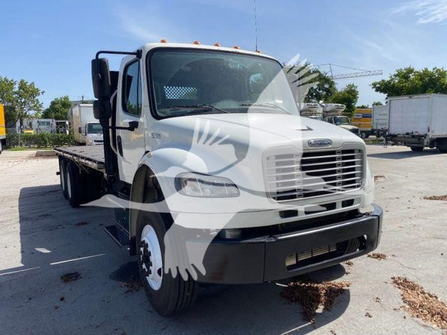 Flatbed truck in front view showing Freightliner M2-106 cab with white paint and black bumper. VIN label not visible. Flatbed chassis visible.