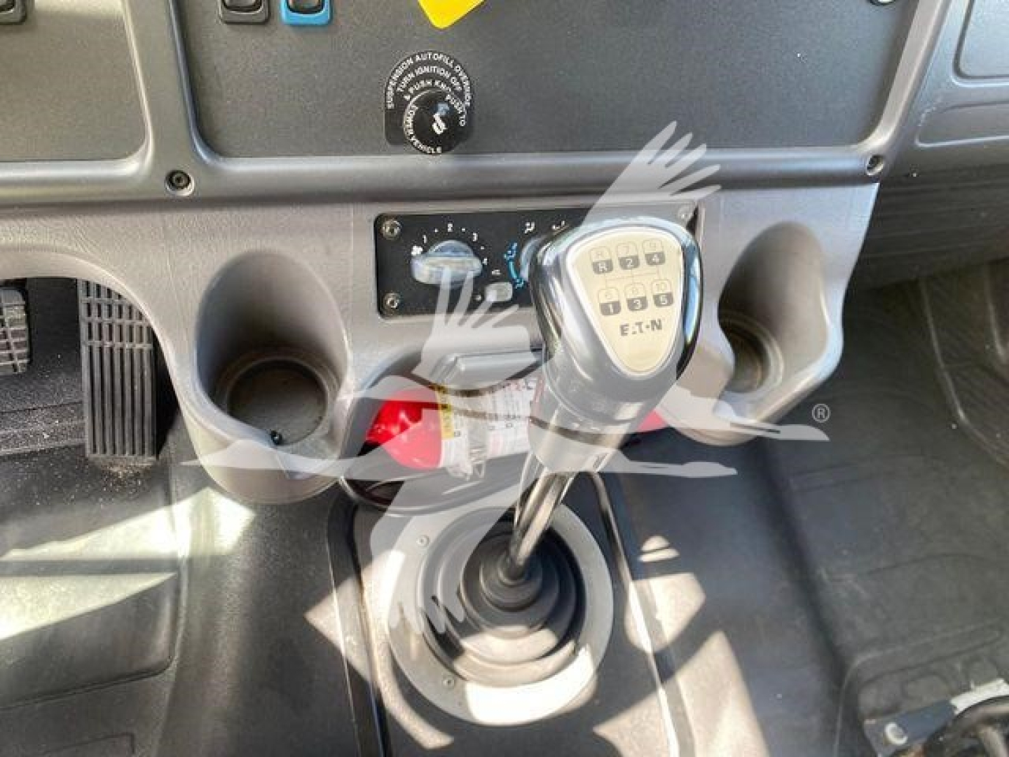Interior of Freightliner M2 106 cab showing manual gear shifter and center console with cup holders and dash controls.