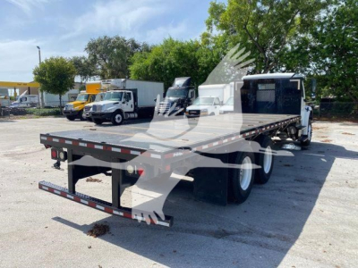 Flatbed truck chassis of a 2018 Freightliner M2 106 viewed from rear-left showing flatbed with reflective tape and rear bumper.