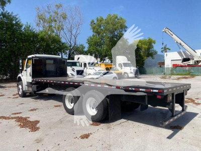 Flatbed truck on a 2018 Freightliner M2 106 chassis showing a long steel flatbed and dual rear axles.