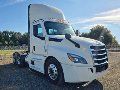 White 2023 Freightliner Cascadia126 conventional daycab tractor from front-left view showing cab, sleeper, and dual rear axles with chrome wheels.