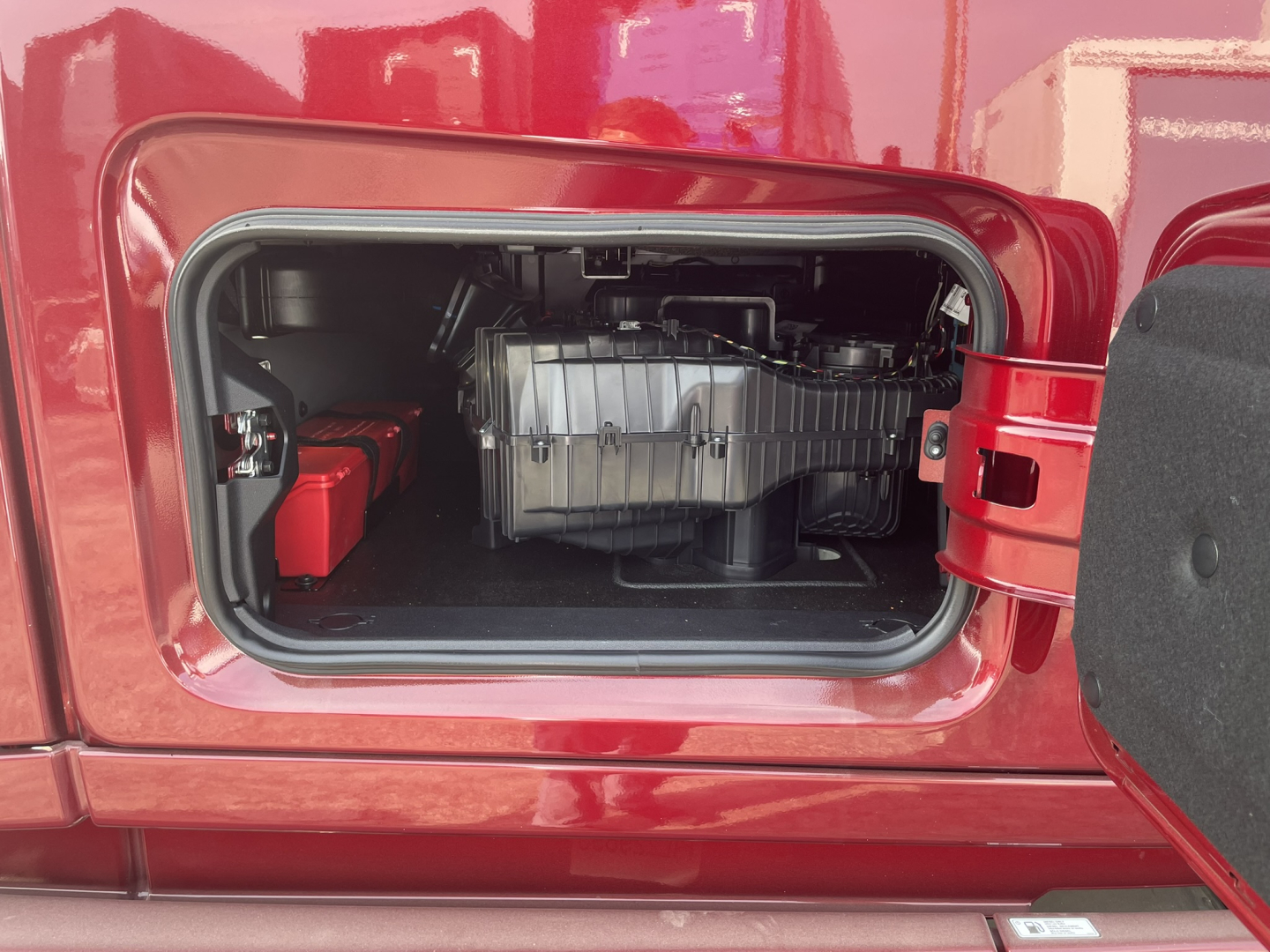 Truck door opening showing engine bay access with a large component and red exterior; appears to be a Volvo VNL64T860 conventional sleeper interior bay view.