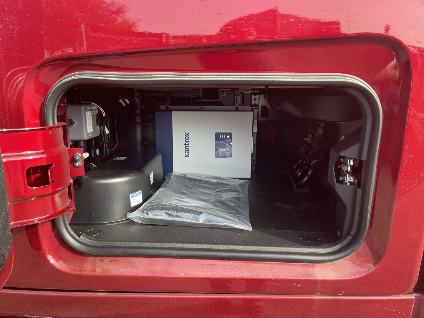 Volvo VNL64T860 cab storage area open showing a boxed XMrytes or similar equipment and a packaged item in the side compartment.