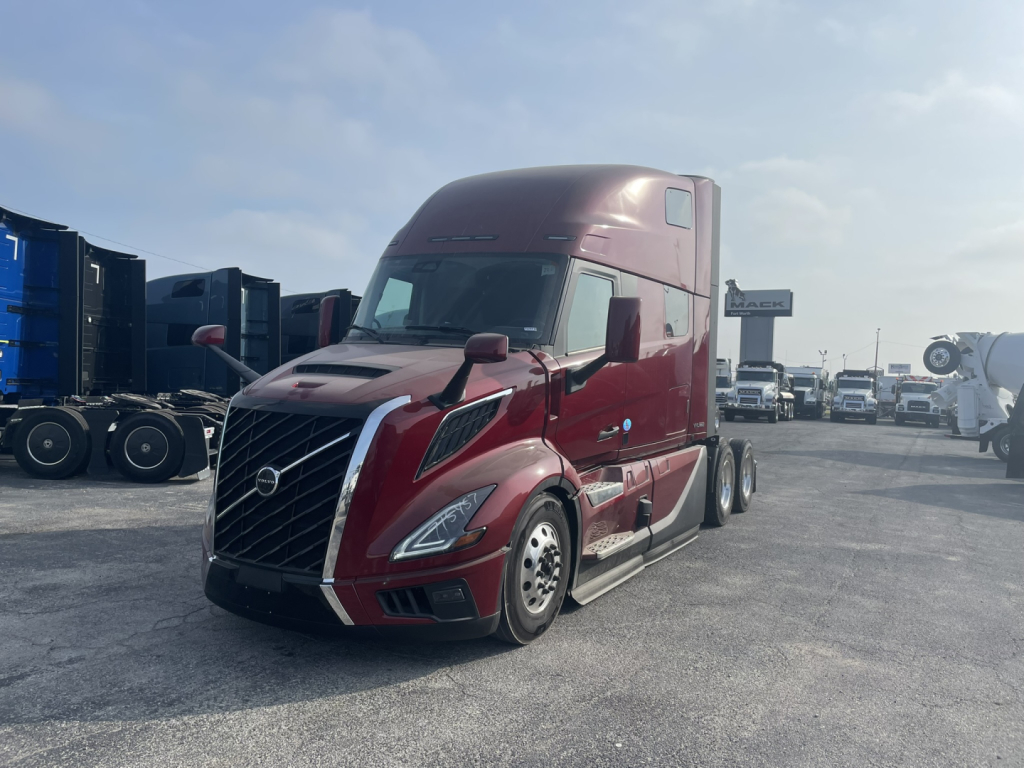 2016 Volvo VNL64T860 sleeper cab tractor in maroon with chrome grille and aerodynamic design, parked in a lot with other trucks.
