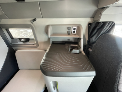 Volvo VNL64T860 cab interior showing sleeper area and window with curtain, storage hatch, and control panel. 