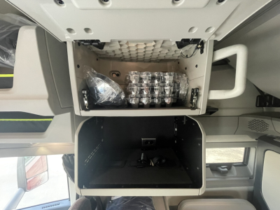 Volvo VNL64T860 sleeper cab interior showing overhead storage with stacked chrome cups and a small bag, plus an open lower compartment.