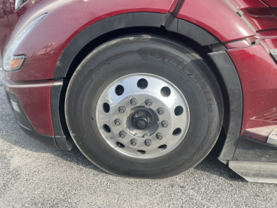 Wheel and fender of a red 2026 Volvo VNL64T860 truck showing a steel wheel with multiple lug nut holes and a black tire.