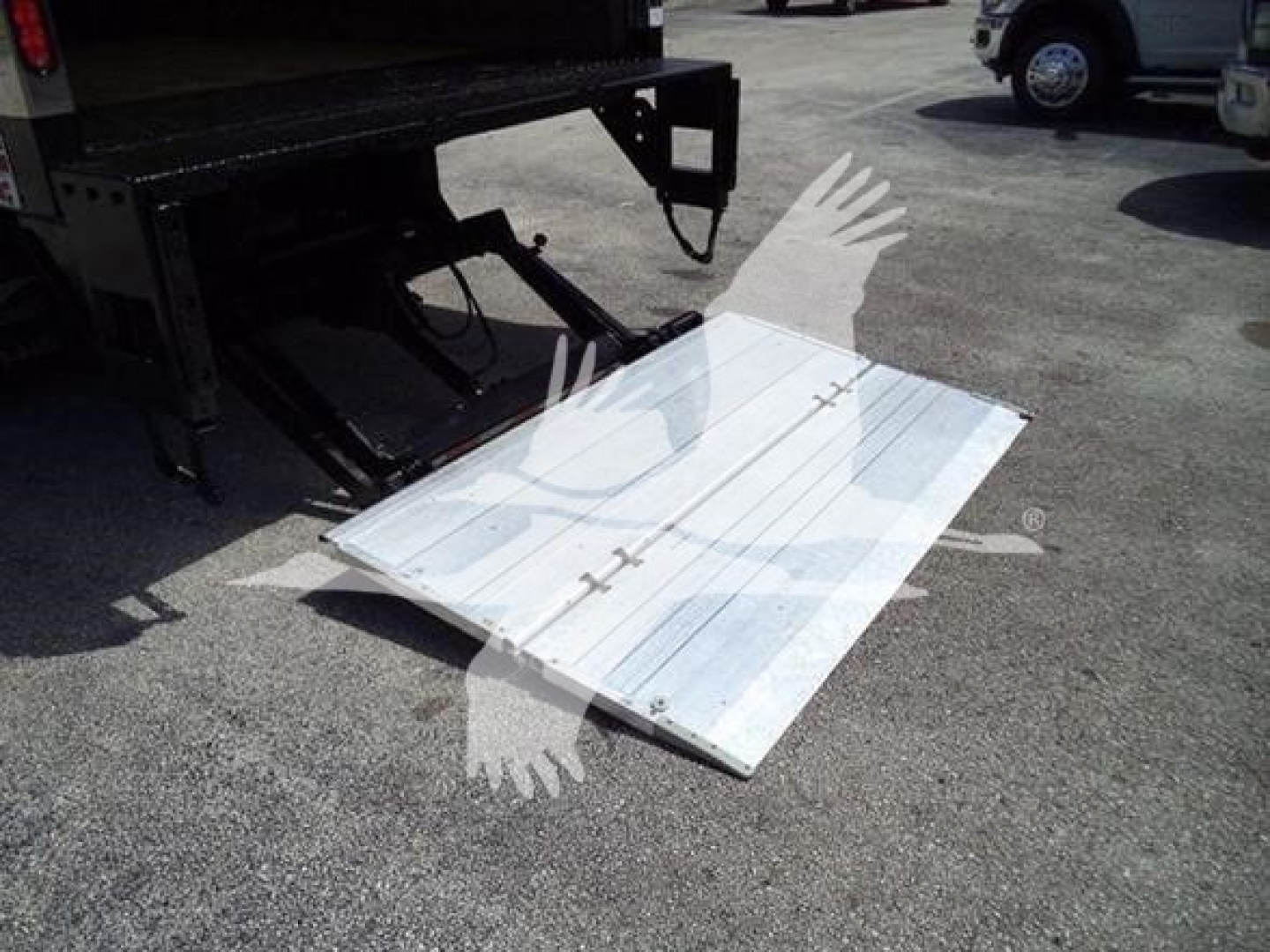 Isuzu NPR HD box truck tailgate ramp folded metal platform with reflective surface near truck hitch and other vehicles in background