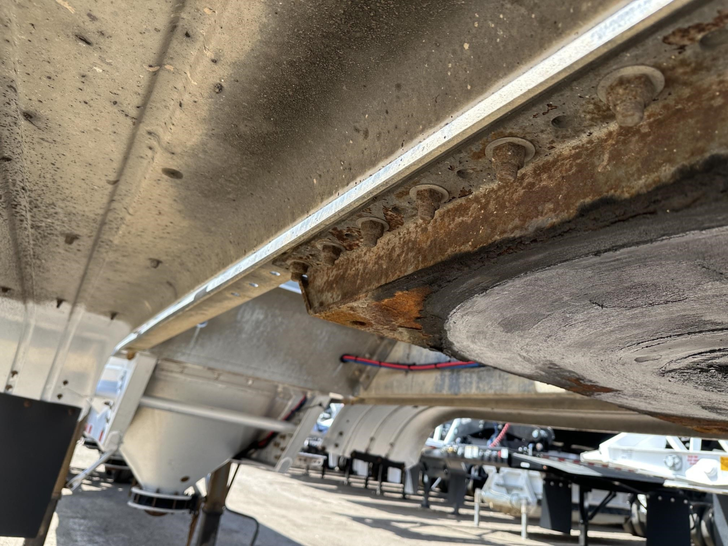 Underbelly of a trailer showing a rusted edge and circular metal plate, with a portion of frame and electrical lines visible.