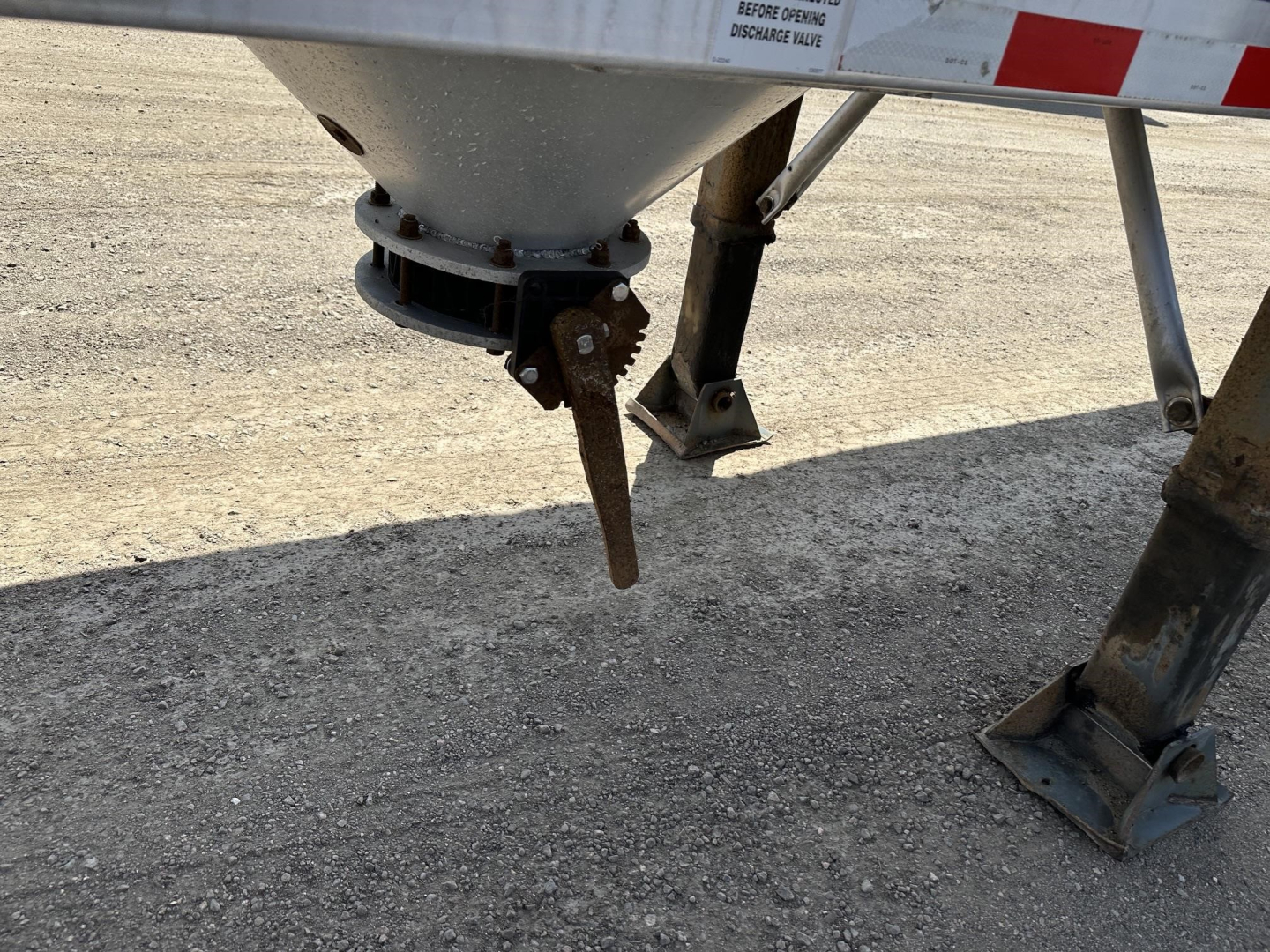 Trailer underside showing gravity drop pneumatic discharge chute with support legs and mounting brackets.