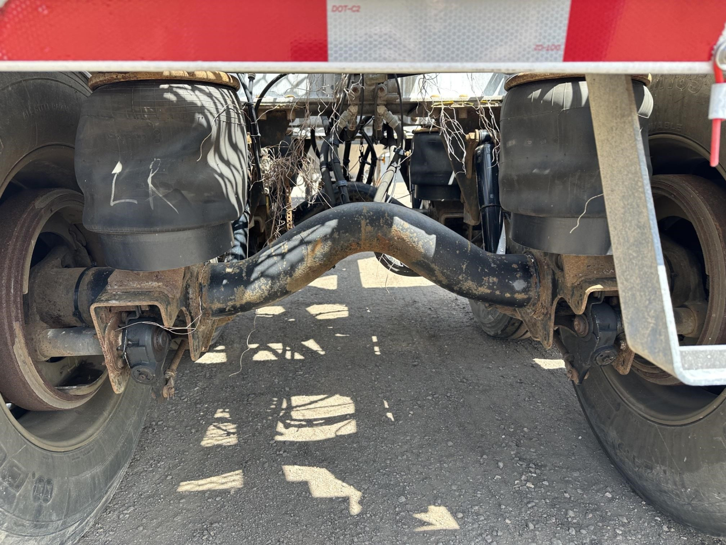 Trailer undercarriage showing pneumatic drop axle with twin-arc suspension and junction hoses. Visible components include hoses, pipes, and wheel hubs.