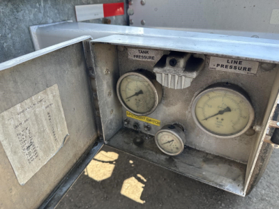 Panel showing tank pressure and line pressure gauges with labels; control knobs and small meter beneath; metal enclosure with worn label and reflective surface.