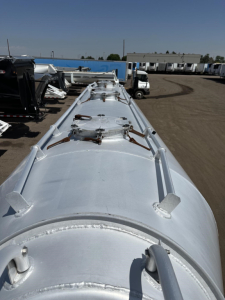 Pneumatic trailer top view showing silvery cylindrical tank with manways and securing latches.