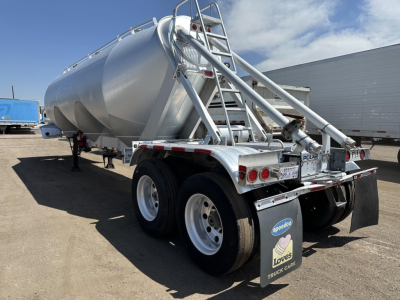 Pneumatic dry bulk trailer showing rear and side with dual tandem axles and polished metal tank, Polaris branding plate, and ladder access.