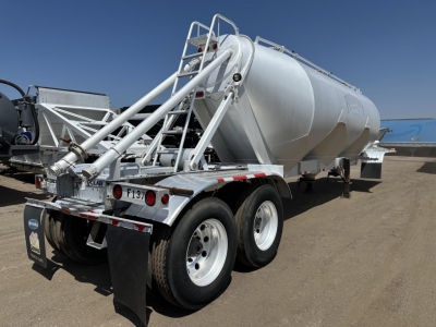 Pneumatic dry bulk trailer with tandem axles and cylindrical silo, rear access ladder, and discharge chute visible.