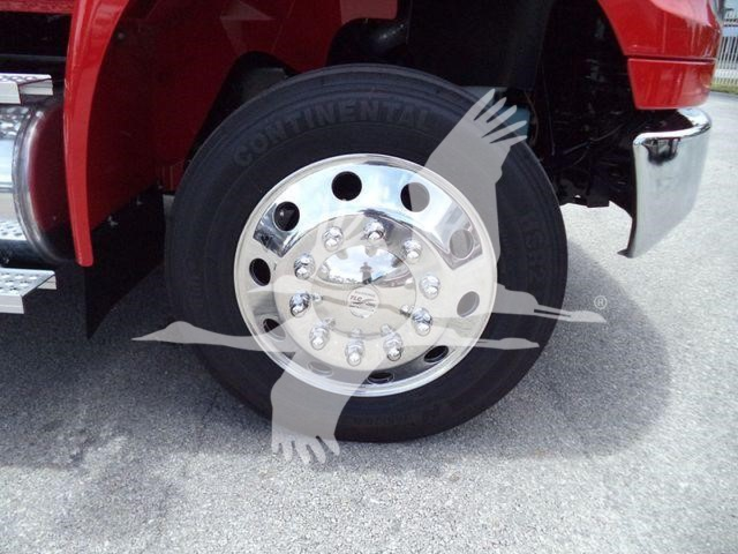 Truck wheel and tire shown with Continental tire brand on black rubber, polished chrome hubcap, red truck fender, chrome bumper; part of rollback truck undercarriage visible.