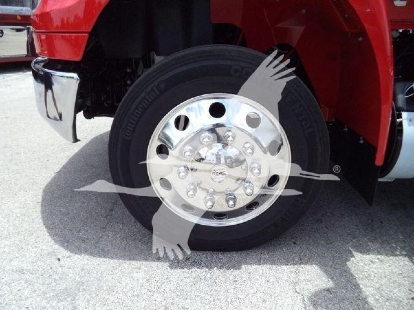 Truck front wheel and chrome hubcap showing wheel and tire with fender and red body panel.