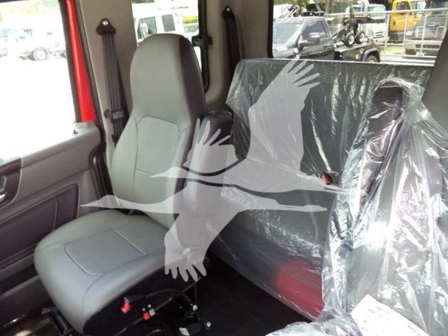 Interior of a new 2027 International MV rollback truck showing driver seat and plastic-covered rear seating with light gray upholstery.