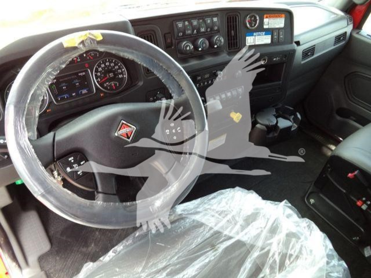 Interior of a 2027 International MV truck cab showing steering wheel, dashboard, and plastic seat cover.